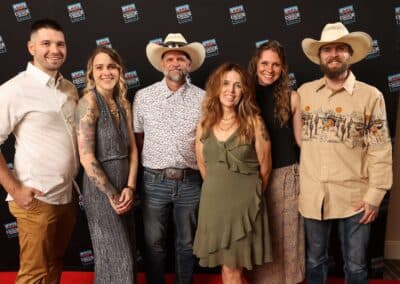 Six members of The Paw Spa Elite team standing together in front of an event backdrop, two in cowboy hats.
